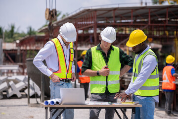 Engineers wearing safety helmets and reflective vests working construction site large overhead crane operation ensure efficient secure handling of heavy materials industrial engineering project.