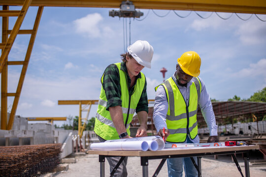 Engineers wearing safety helmets and reflective vests working construction site large overhead crane operation ensure efficient secure handling of heavy materials industrial engineering project. - Powered by Adobe
