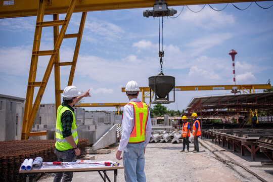 Engineers wearing safety helmets and reflective vests working construction site large overhead crane operation ensure efficient secure handling of heavy materials industrial engineering project.