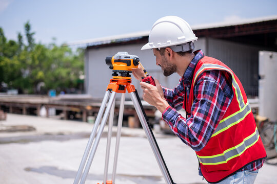 Construction surveyors wearing safety helmets and reflective vests working on site using theodolite and leveling rod measure land align structures precision during a civil engineering project