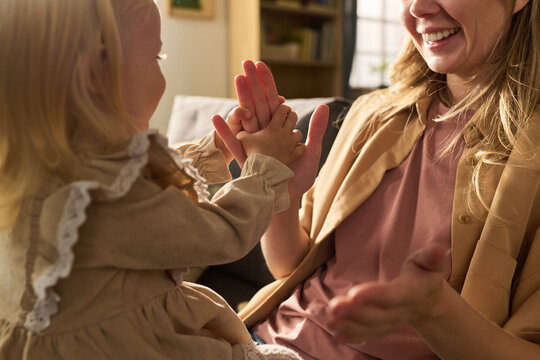 Caucasian woman smiling while playing hand clapping game with Caucasian child indoors, both engaging in interactive activity, child facing woman, joyful expressions visible