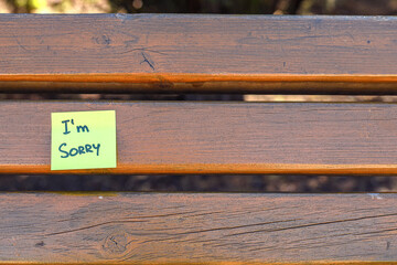 “I’m Sorry” Note on Wooden Bench. Green sticky note with handwritten “I’m sorry” message placed on a wooden bench. Symbol of apology, forgiveness, and emotional honesty.