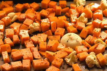 Diced Baked Vegetables on Wooden Table. Close-up of roasted diced vegetables, including sweet...