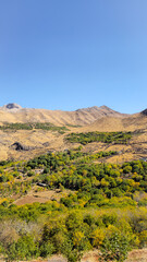 Naklejka premium Autumn mountain valley with dry soil, golden foliage, and rugged peaks under clear blue sky — a vivid seasonal contrast. 📍Hazarani, Hawraman