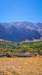 Naklejka premium Autumn mountain valley with dry soil, golden foliage, and rugged peaks under clear blue sky — a vivid seasonal contrast. 📍Hazarani, Hawraman