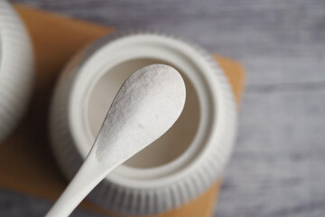 White sugar on a spoon next to a container on a table