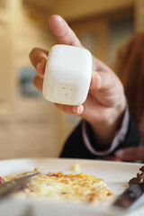 Person seasoning food with salt shaker in a cozy restaurant