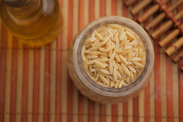 Rice shaped pasta and olive oil on a wooden table