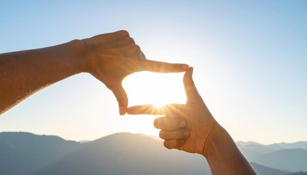Hands forming a frame around the sun creating a picturesque landscape focus