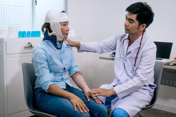 Obraz premium A male doctor gently examines and reassures an Asian female patient wearing a head bandage and neck brace after an accident,reflecting empathy, recovery care,professional medical support in a clinic