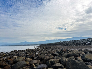 Rocky shoreline meets distant mountains under a vast expressive cloudy sky landscape
