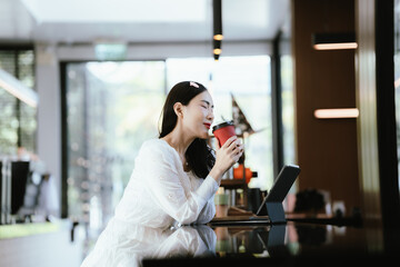 A woman relaxing in a modern café, enjoying a hot drink while sitting at the counter with a tablet nearby, looking thoughtful and content.