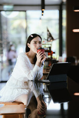 A woman relaxing in a modern café, enjoying a hot drink while sitting at the counter with a tablet nearby, looking thoughtful and content.
