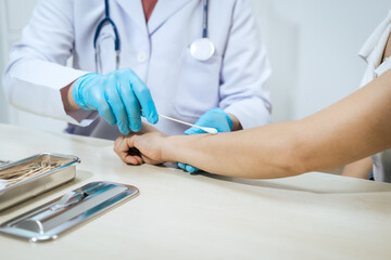 Asian male doctor cleans and treats a female patient&rsquo;s arm wound with antiseptic before injection or medical procedure, wearing blue gloves in a clean and sterile clinical environment