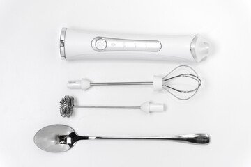 Electric mixer with attachments and spoon on white surface