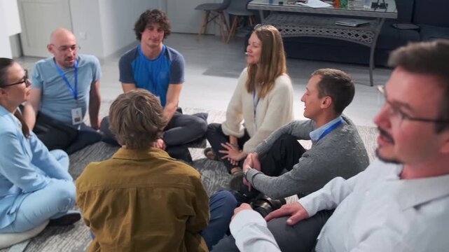 Employees takes part in psychological training session led by corporate coach. Sitting in circle with closed eyes, colleagues perform relaxation, breathing exercises by raising and lowering hands.