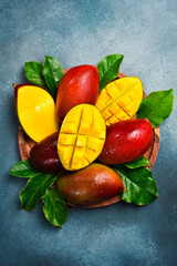 Set of ripe mango fruits and leaves on a wooden plate. On a concrete stone background. Tropical fruits.