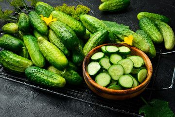 Sliced fresh green cucumber in a wooden bowl and a set of fresh cucumbers on the table. On a stone table background. Top view.