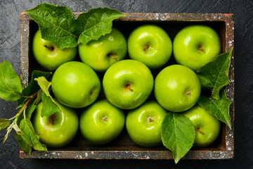Wooden box with apples. Juicy green apples with leaves. Close-up. On a black stone background.