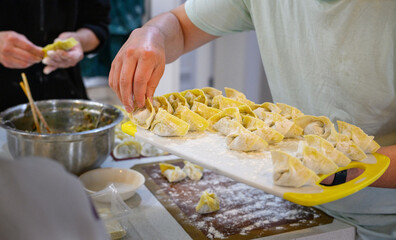 Hands of people making wontons on the kitchen table.