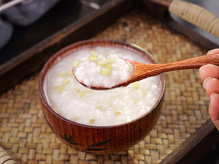 Traditional Asian Congee Rice Porridge with Green Kernels in Wooden Bowl