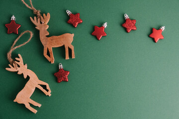 A minimalist Christmas or New Year's background with deer and red stars. Wooden deer figurines on a green background.