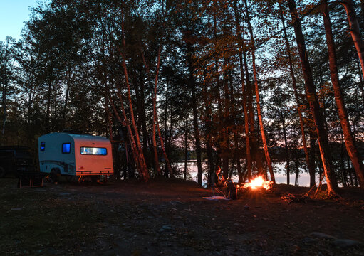 RV Camper on shore of lake with campfire at dusk, Maine