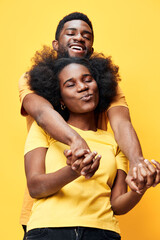 Obraz premium Joyful couple with Afro hairstyles wearing matching yellow shirts against a bright yellow background, showcasing love and happiness