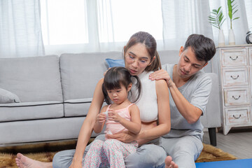 Beautiful pregnant woman and keeping eyes closed sitting on yoga mat while father assisting mom in practicing yoga pose in livingroom, family spendtime together, young female working out at home.
