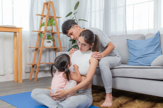 Beautiful pregnant woman and keeping eyes closed sitting on yoga mat while father assisting mom in practicing yoga pose in livingroom, family spendtime together, young female working out at home. - Powered by Adobe