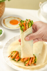 Handmade healthy vegetable wrap with fresh ingredients held in hand during nutritious breakfast meal