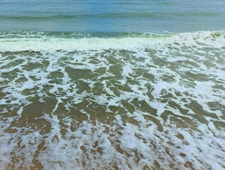 Amazing view of the sea wave breaking on the coast and covering the sandy beach with its foam.