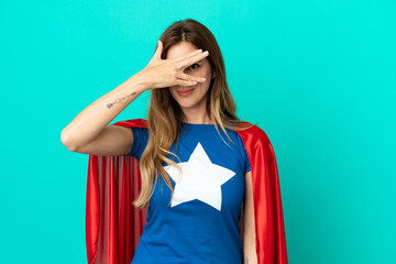 Super Hero caucasian woman isolated on blue background covering eyes by hands and smiling