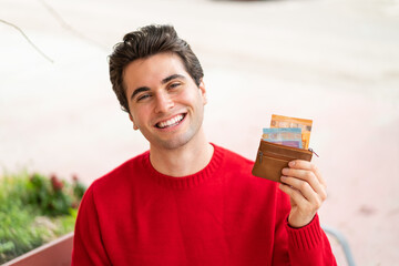 Young handsome man holding wallet with money with happy expression