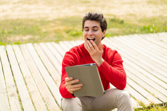 Young handsome man holding a tablet at outdoors with surprise and shocked facial expression