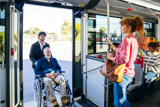 Young man assisting a senior individual in a wheelchair getting onto a public transport bus, showing urban accessibility
