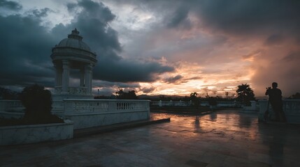 Dramatic sunset illuminates a wet plaza and white pavilion observed by a silhouette photographer