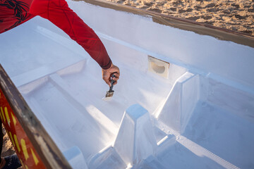 Doha, Qatar - March 14, 2025: Painting the interior of a dragon boat with white paint on a sandy beach