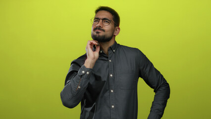 Young man wearing glasses scratching head in thoughtful pose isolated on yellow background