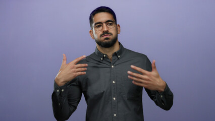 Young hispanic man with glasses posing against a purple background, wearing a dark shirt, looking expressive and thoughtful.
