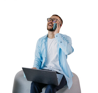 Young businessman sitting on transparent background room using laptop talks by phone smiling eyes closed happy after receiving great news. Successful people, financial triumph. Excited guy at home.