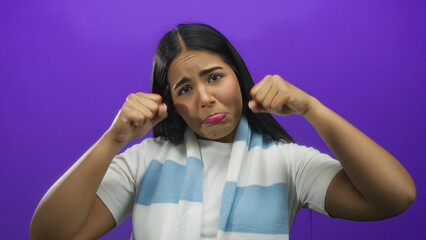 Young latin woman playfully pouting against a vibrant purple background, wearing a white shirt and light blue scarf, creating a fun and expressive mood.