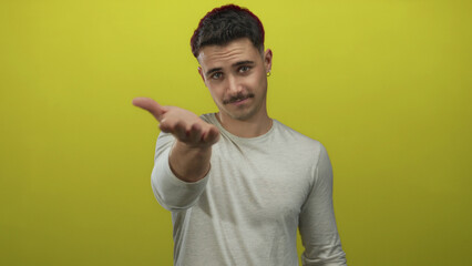 Young hispanic man presenting hand against vivid yellow background, conveying openness and...
