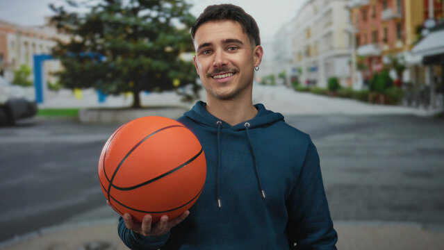 Young man holding basketball on city street in outdoor setting, showcasing urban lifestyle and sports passion.