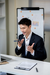 A businessman is talking to an AI via smartphone on his desk in an office.