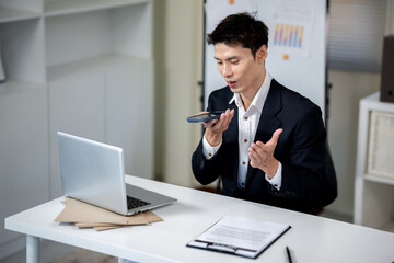 A businessman is talking to an AI via smartphone on his desk in an office.
