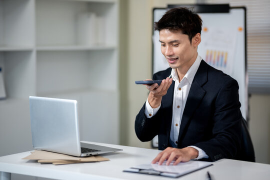 A businessman is talking to an AI via smartphone on his desk in an office.