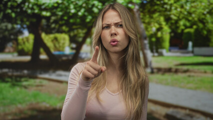 Fototapeta premium Woman points index finger forward on city park path with focused gaze and visible hand gesture; anger scolding warning.