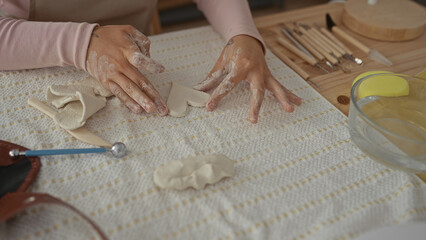 Woman hands shaping clay into heart forms on a wooden table with water bowl and clay tools in pottery studio; creativity focus.