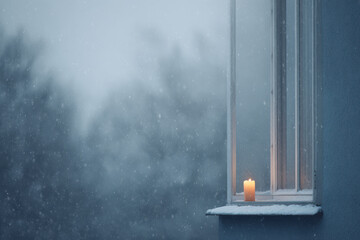 snowflakes gently falling on glass window reflecting warm glow of candle inside creating cozy winter atmosphere